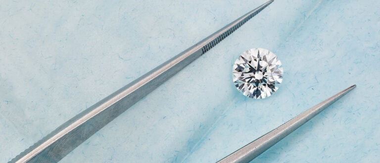 Lab-grown diamond with tweezers on blue background, showcasing sustainable jewelry options.