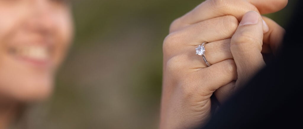 Brilliant lab-grown diamond engagement ring on woman's hand at outdoor setting.